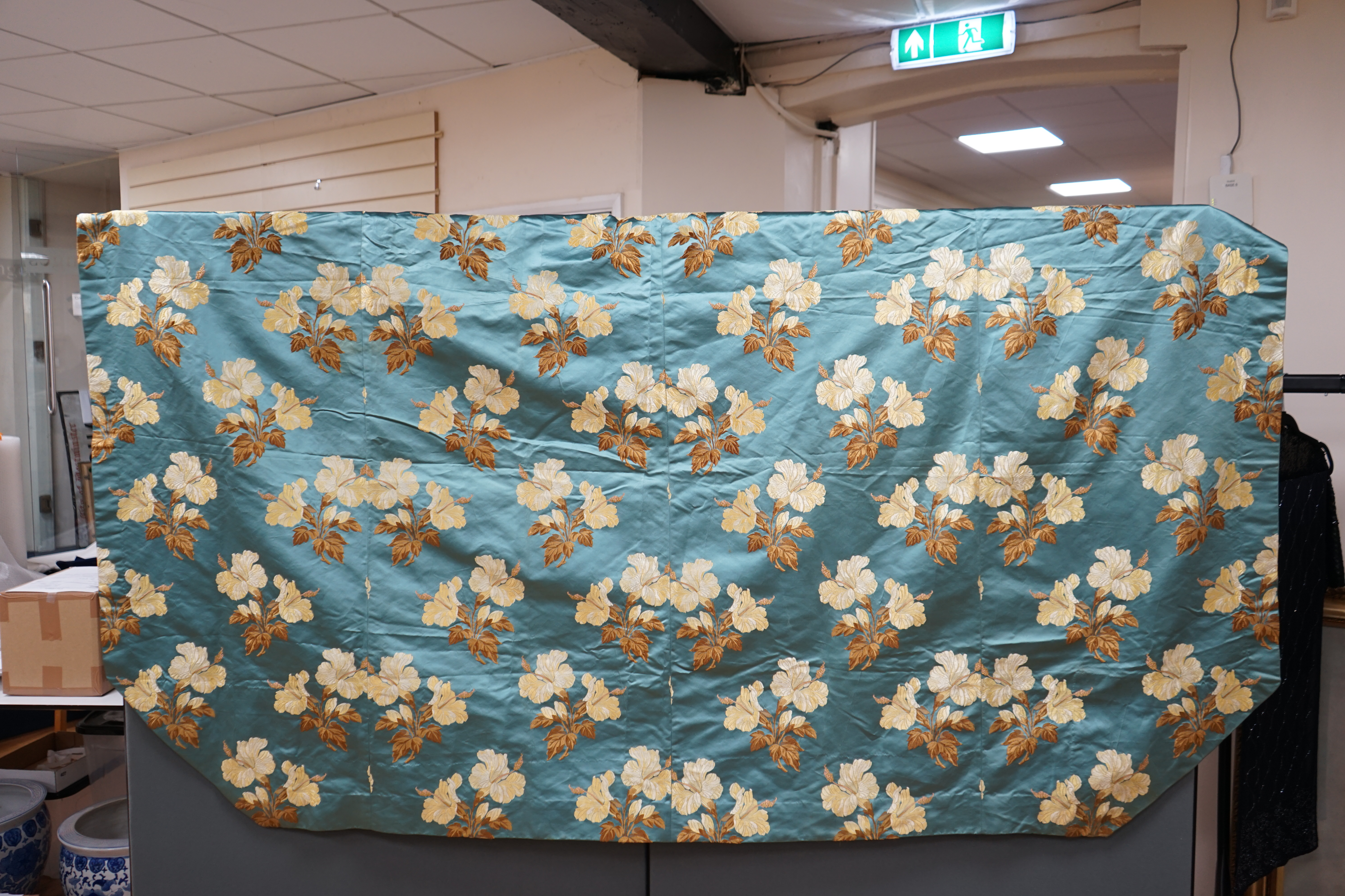 A turquoise satin floral silk brocaded panel of four 59cm widths, boldly embroidered in yellow and brown strays of lilies, the panel possibly part of a pelmet or half tester bed, each spray being 21cm high as a diagonal